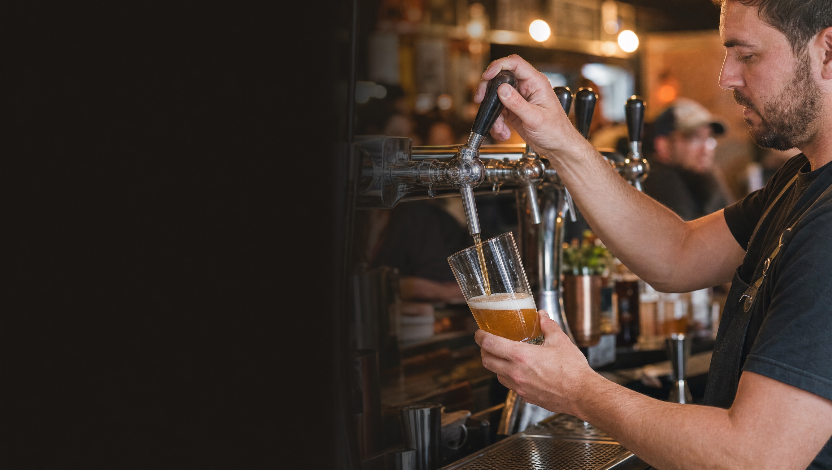 A bartender pours a draft beer in a warmly lit restaurant.